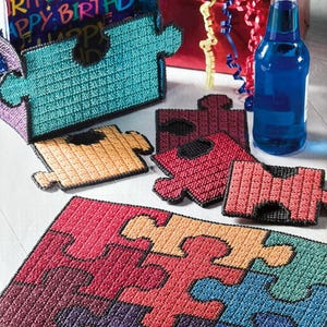 May include: A set of colourful puzzle-shaped coasters with a red, orange, yellow, green, blue, purple and black colour scheme. The coasters are made of plastic canvas and are perfect for adding a touch of whimsy to any home decor.