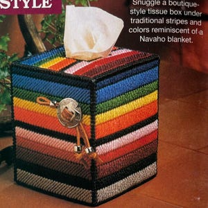 Könnte beinhalten: Ein quadratischer Taschentuchbox-Überzug aus Kunststoffgewebe mit horizontalen Streifen in Blau, Grün, Gelb, Orange, Pink, Braun und Schwarz. Ein silberfarbener, runder Concho-Knopf mit Lederband und Metallperlen ist an der Vorderseite befestigt.