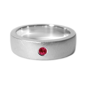 May include: A silver band ring with a small, round, red gemstone set in the center.