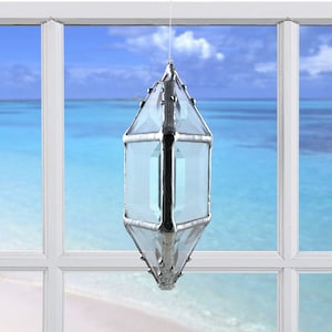 May include: A silver, faceted, crystal prism hanging in a window with a view of a beach and ocean.