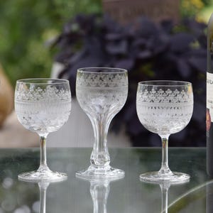 May include: Four clear glass stemmed glasses featuring an etched decorative pattern around the upper rim, positioned next to a dark bottle of Taylor Fladgate 10 Year Old Tawny Porto wine with a white label and black text detailing the contents.