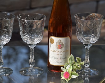 Może przedstawiać: Cztery przezroczyste szklane kieliszki do wina z butelką wina Marco Donati Pinot Grigio Ramato w środku. Butelka ma złotą etykietę z nazwą winnicy i rokiem 1963.