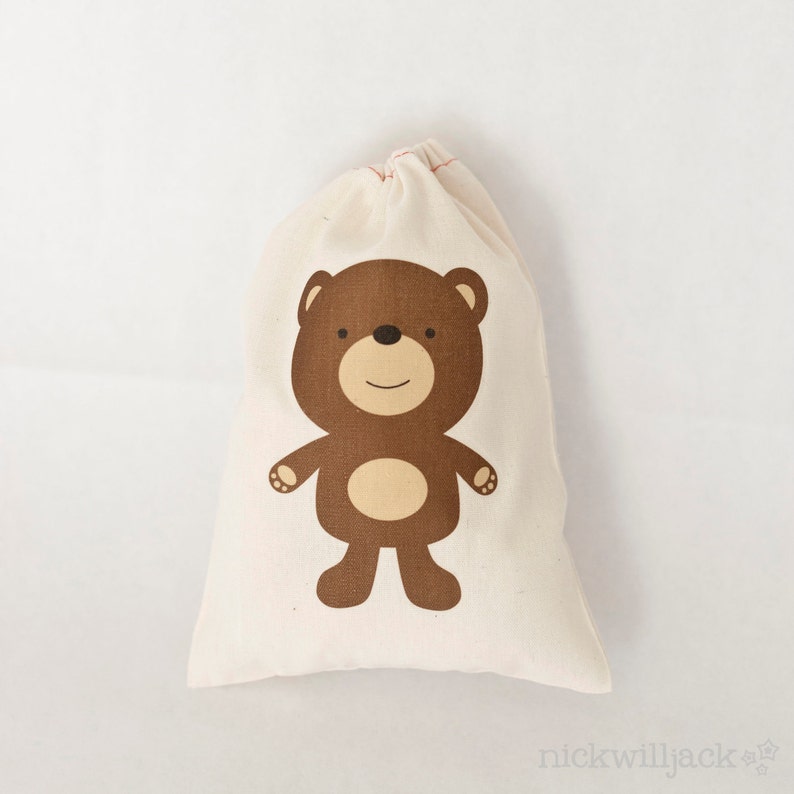 May include: A small, white cotton drawstring bag with a brown bear illustration. The bear has a brown nose, brown eyes, and a light brown belly.
