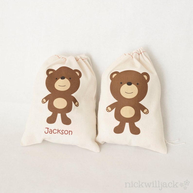 May include: Two brown canvas bags with a brown bear illustration and red stitching. The bag on the left has the name "Jackson" printed on it.