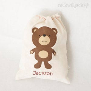 May include: A white cotton drawstring bag with a brown bear illustration and the name "Jackson" printed on the front.