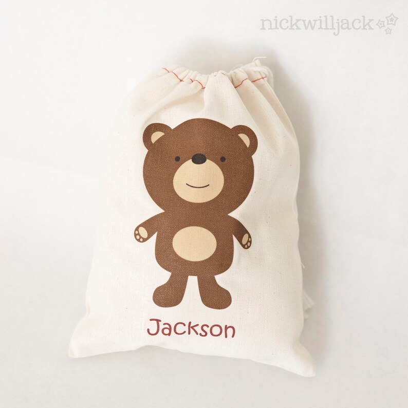 May include: A white cotton drawstring bag with a brown bear illustration and the name "Jackson" printed on the front.