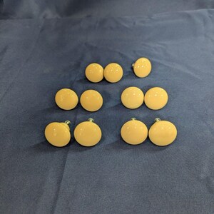 May include: A collection of nine round, smooth, light beige cabinet knobs with a glossy finish. Each knob features a simple, circular design with a metallic screw attachment visible on the underside, arranged in a grid-like pattern on a dark surface.