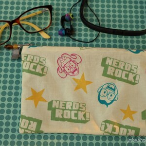May include: A white fabric pouch with a zipper closure. The pouch has a repeating pattern of stars, cartoon characters, and the text "Nerds Rock!" in green, blue, and pink.