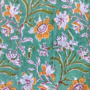May include: A close-up of a fabric with a floral pattern. The design features yellow, white, and pink flowers with green leaves and stems against a light green background. The flowers are stylized and evenly spaced.
