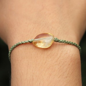 May include: A green string bracelet with a yellow citrine gemstone.