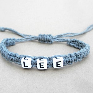 A personalized gray braided hemp bracelet with white letter beads that spell out the name 'LEE'.