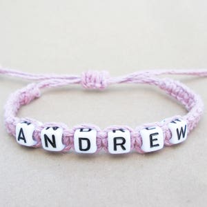 A customized pink hemp string bracelet with white letter beads that spell out the name 'ANDREW'.