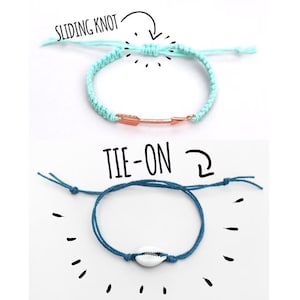 Two bracelets, one light blue and one dark blue, with different closures. The light blue bracelet has a sliding knot closure and a gold arrow charm. The dark blue bracelet has a tie-on closure and a white seashell charm. The text 'SLIDING KNOT' and 'TIE-ON' are written above the bracelets.