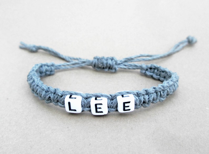 A personalized gray braided hemp bracelet with white letter beads that spell out the name 'LEE'.