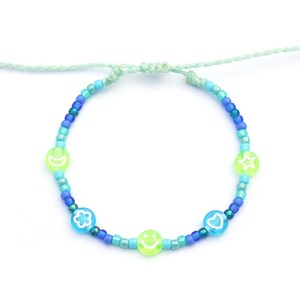 May include: A blue and green beaded bracelet with a smiley face, heart, star, and flower charm. The bracelet is made with small, colorful beads and has a light green string.