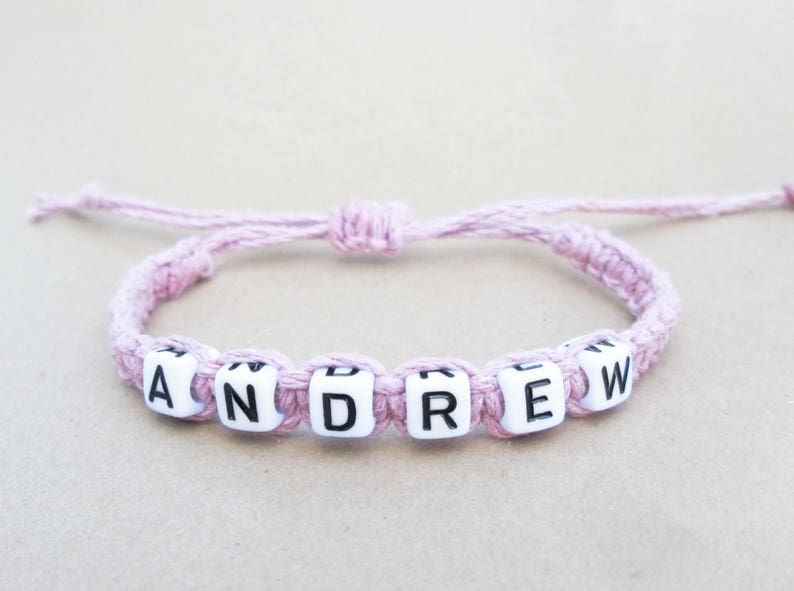 A customized pink hemp string bracelet with white letter beads that spell out the name 'ANDREW'.