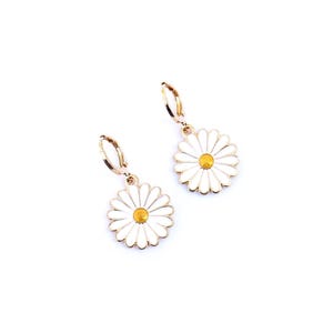 May include: A pair of gold-tone earrings with white daisy flower charms. The earrings have a hoop design.