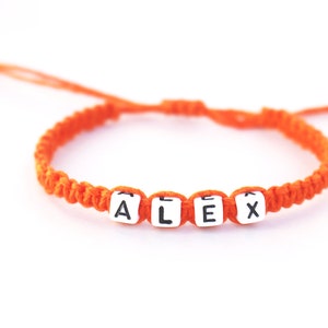 A personalized orange hemp string bracelet with white letter beads that spell out the name 'ALEX'.