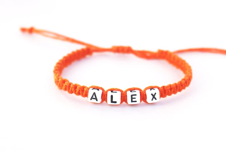 A personalized orange hemp string bracelet with white letter beads that spell out the name 'ALEX'.