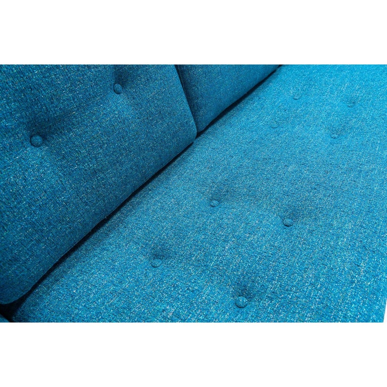 May include: Close-up of a teal blue sofa with button tufting. The fabric has a subtle texture.