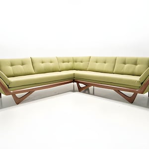 May include: A green sectional sofa with a wood frame and angled legs. The sofa has a tufted back and is upholstered in a soft fabric.