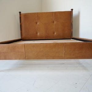May include: A brown leather bed frame with a tufted headboard and wooden legs. The bed frame is made of solid wood and has a classic design.