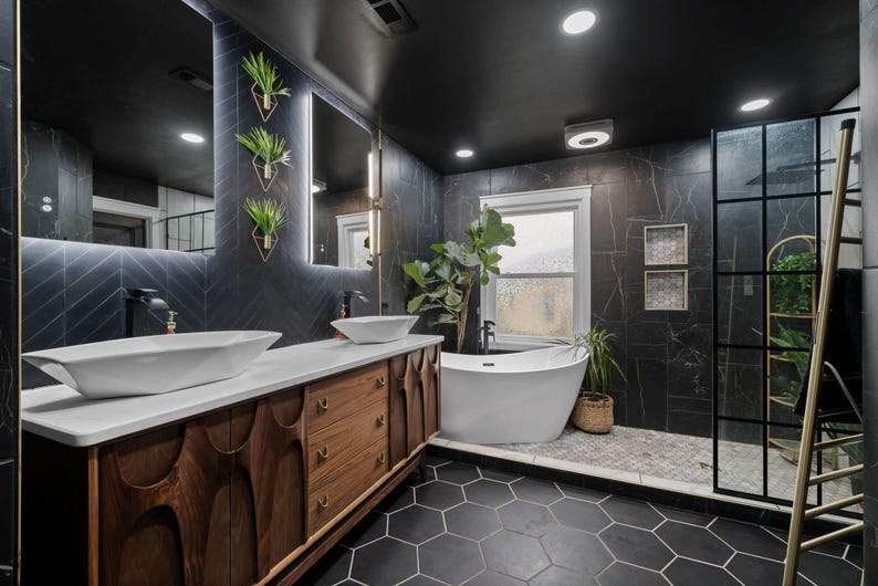 K&ouml;nnte beinhalten: Ein modernes Badezimmer mit schwarzen Fliesenw&auml;nden, einer freistehenden wei&szlig;en Badewanne und einem Doppelwaschtisch mit einer Holztheke und zwei wei&szlig;en Waschbecken. Das Badezimmer verf&uuml;gt &uuml;ber ein gro&szlig;es Fenster, eine Dusche mit Glast&uuml;r und eine goldene Leiter.