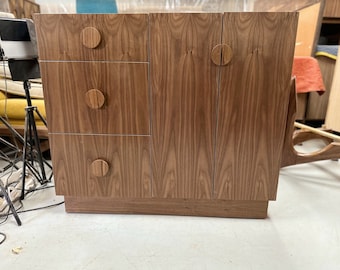 May include: A wooden cabinet with three drawers and two doors. The cabinet has a light brown finish and round wooden knobs.