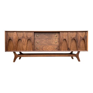 May include: Mid-century modern walnut sideboard with three drawers and two doors. The doors have a unique carved design and the sideboard has brass hardware.