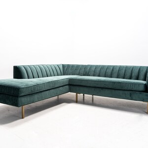May include: A teal green sectional sofa with a chaise lounge and gold metal legs. The sofa has a tufted design and is upholstered in a soft fabric.