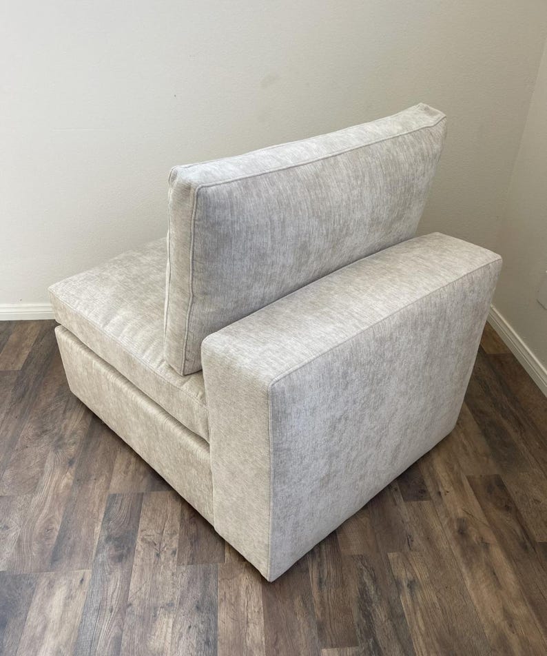 May include: A light gray fabric armchair with a single armrest and a back cushion. The chair is sitting on a wood floor.