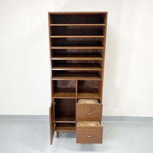 Pu&ograve; includere: Un mobile alto in legno in stile moderno di met&agrave; secolo con pi&ugrave; ripiani e cassetti. Il mobile &egrave; in legno marrone scuro e ha una porta aperta e due cassetti aperti. I cassetti hanno maniglie color oro. Il mobile &egrave; progettato per inclinarsi leggermente all'indietro.