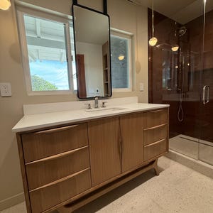 May include: A light wood bathroom vanity with a white countertop, integrated sink, and chrome faucet. The vanity features three drawers on the left, two doors in the center, and three drawers on the right, all with curved wooden handles.