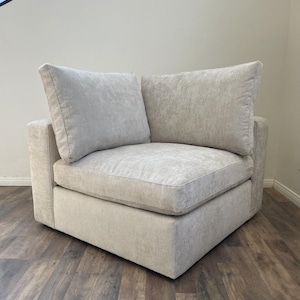 May include: A light gray corner sectional sofa with two plush cushions. The sofa has a tufted fabric upholstery and a square shape.