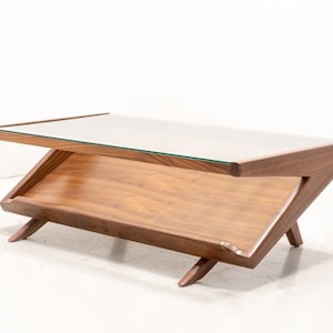 May include: A mid-century modern coffee table with a glass top and a lower shelf. The table is made of wood and has a dark brown finish.
