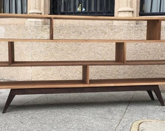 May include: A wooden bookshelf with a unique asymmetrical design. It has multiple shelves and a dark brown base with angled legs.