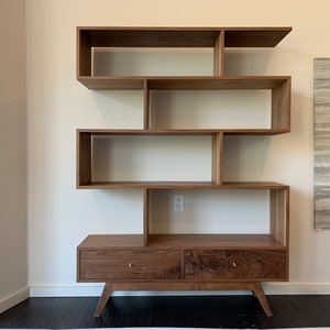 May include: A wooden bookcase with a unique design featuring open shelves and two drawers. The bookcase is made of dark wood and has a modern style.