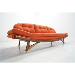 May include: A mid-century modern sofa with a curved wooden frame and orange fabric upholstery. The sofa has a low profile and features a unique design with angled legs.