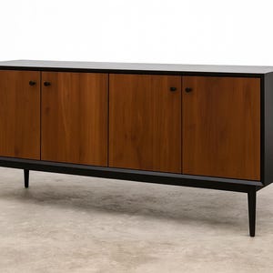 May include: A modern wooden sideboard with four doors and black hardware. The doors are a warm brown color, contrasting with the black frame and legs. The cabinet is a low, rectangular design.