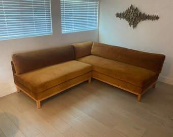 Puede incluir: Un sofá de esquina grande de color amarillo mostaza con un marco de madera. El sofá está hecho de una tela suave y mullida y tiene un diseño moderno.
