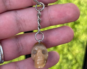 May include: A brown and white skull keychain made of stone. The skull is attached to a silver chain and ring.