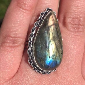 May include: A silver ring with a large teardrop-shaped labradorite gemstone. The ring has a braided silver band.