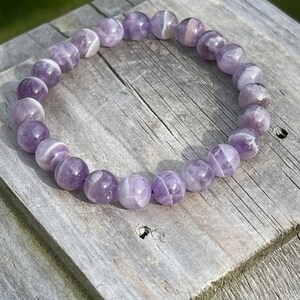 May include: A purple amethyst gemstone bracelet with round beads. The bracelet is made of natural stones and has a polished finish.