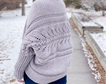 May include: A light purple knitted cardigan with a cable knit pattern and a loose fit. The cardigan is worn by a person with purple hair and is shown from the back.