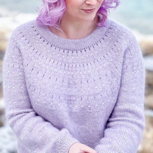 Könnte beinhalten: Ein helllila gestrickter Pullover mit einem zarten perlenartigen Muster. Der Pullover hat einen runden Ausschnitt und lange Ärmel.