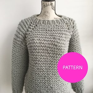May include: A gray knitted sweater with a round neckline and long sleeves. The sweater is on a mannequin. The word "PATTERN" is written in white on a pink circle.