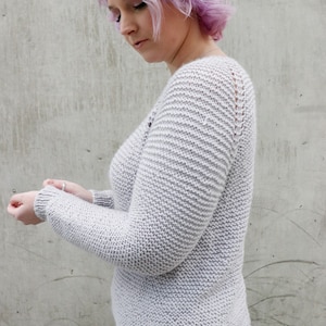 May include: A light gray knitted sweater with a v-neck and long sleeves. The sweater has a textured knit pattern.
