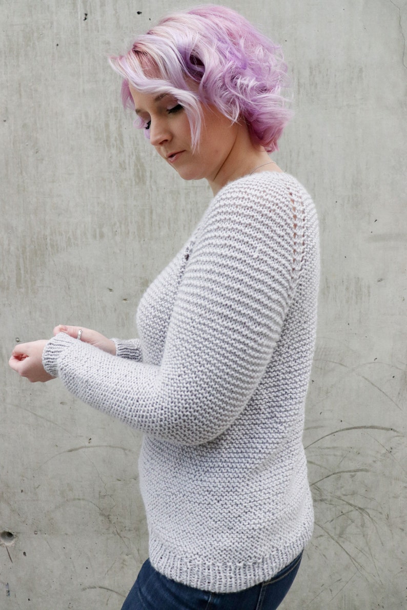 May include: A light gray knitted sweater with a v-neck and long sleeves. The sweater has a textured knit pattern.