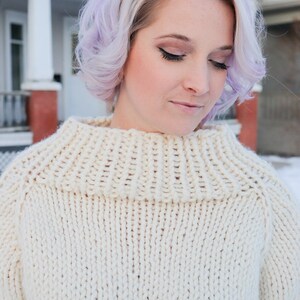 May include: A woman with lavender hair wearing a white knitted turtleneck sweater.