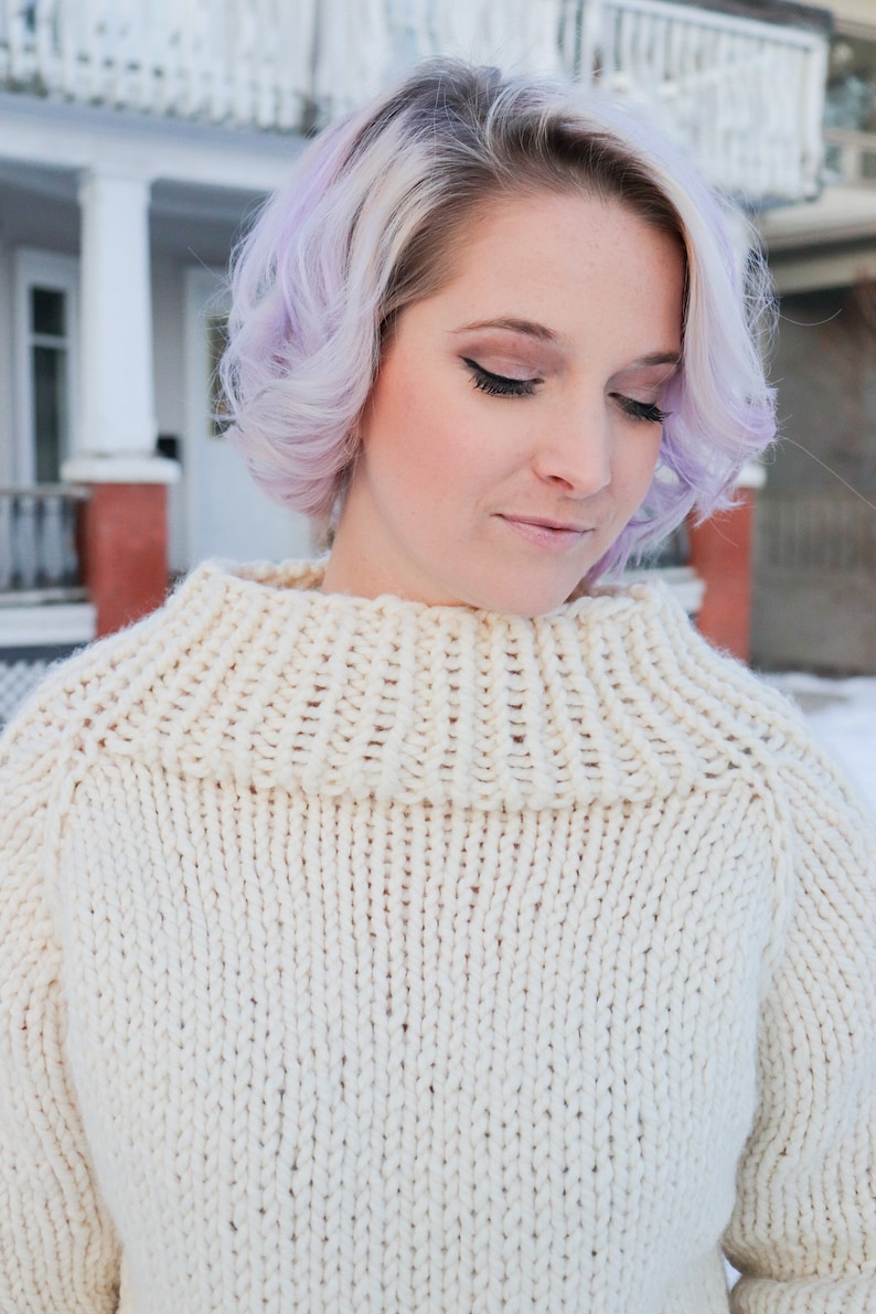 May include: A woman with lavender hair wearing a white knitted turtleneck sweater.